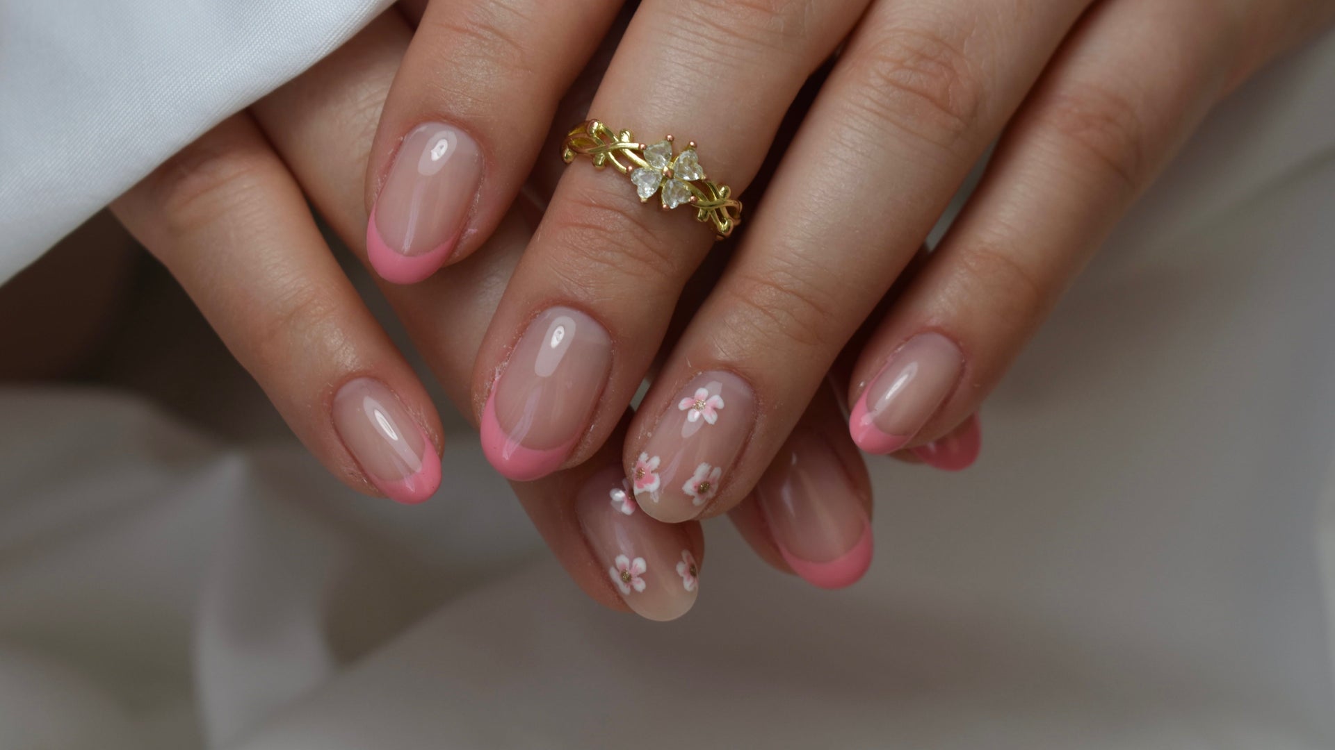 Nagels met een roze french tip en kleine witte bloemetjes, gouden ring