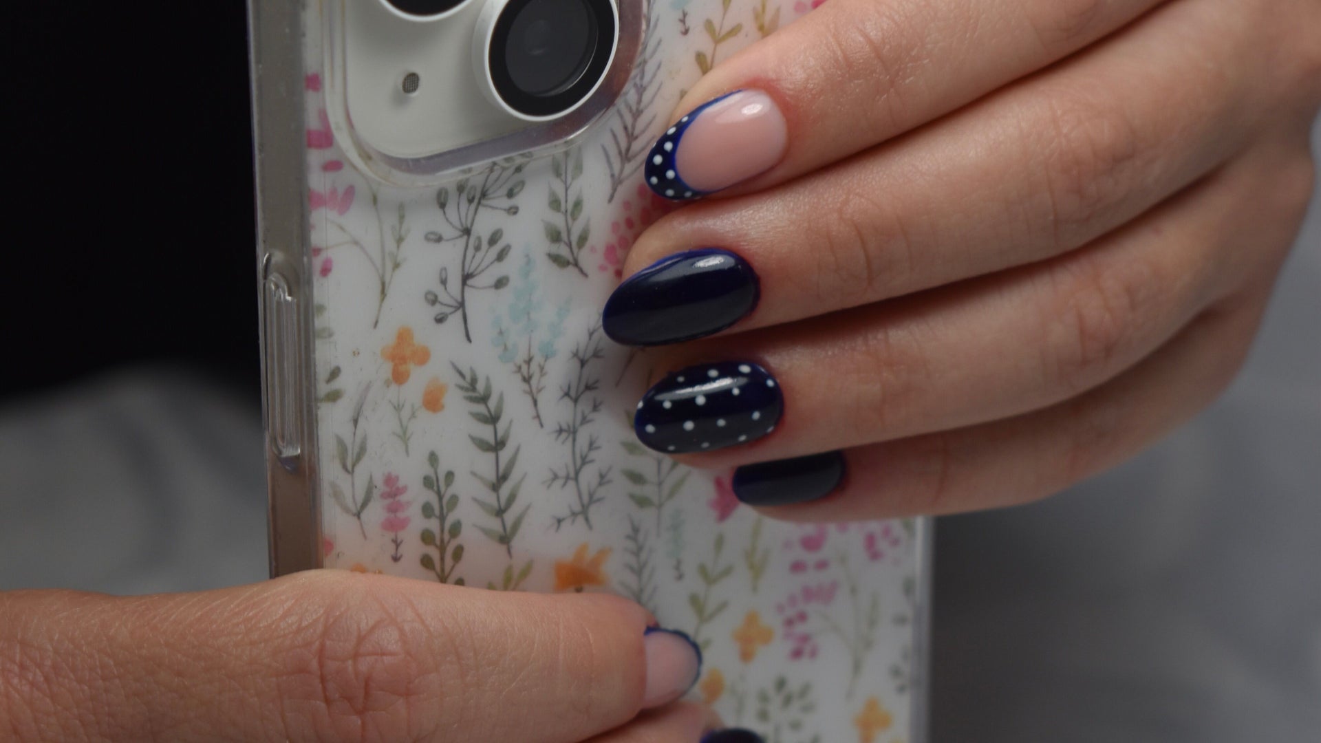 Donkerblauwe nagels met witte stippen, hand met een telefoonhoesje met bloemen