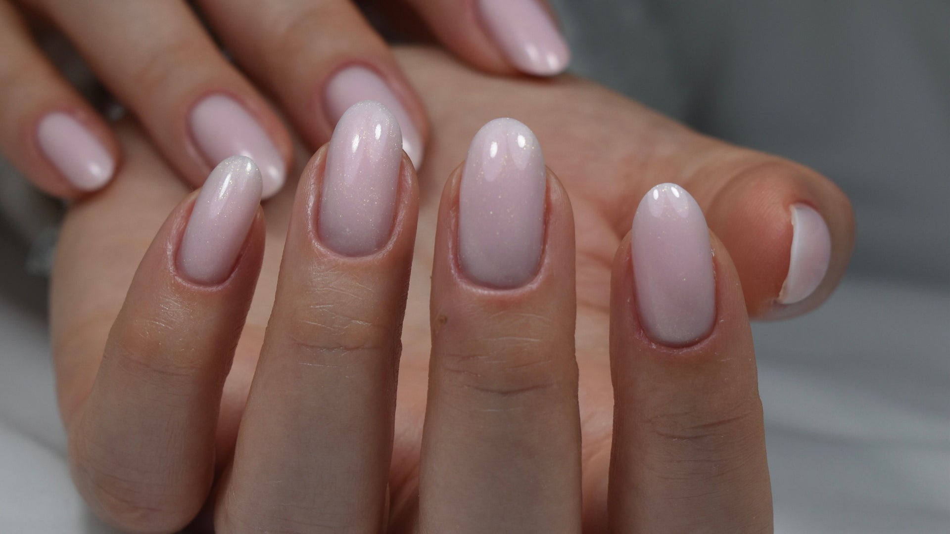 Glanzende, melkroze nagels in amandelvorm op een hand, close-up