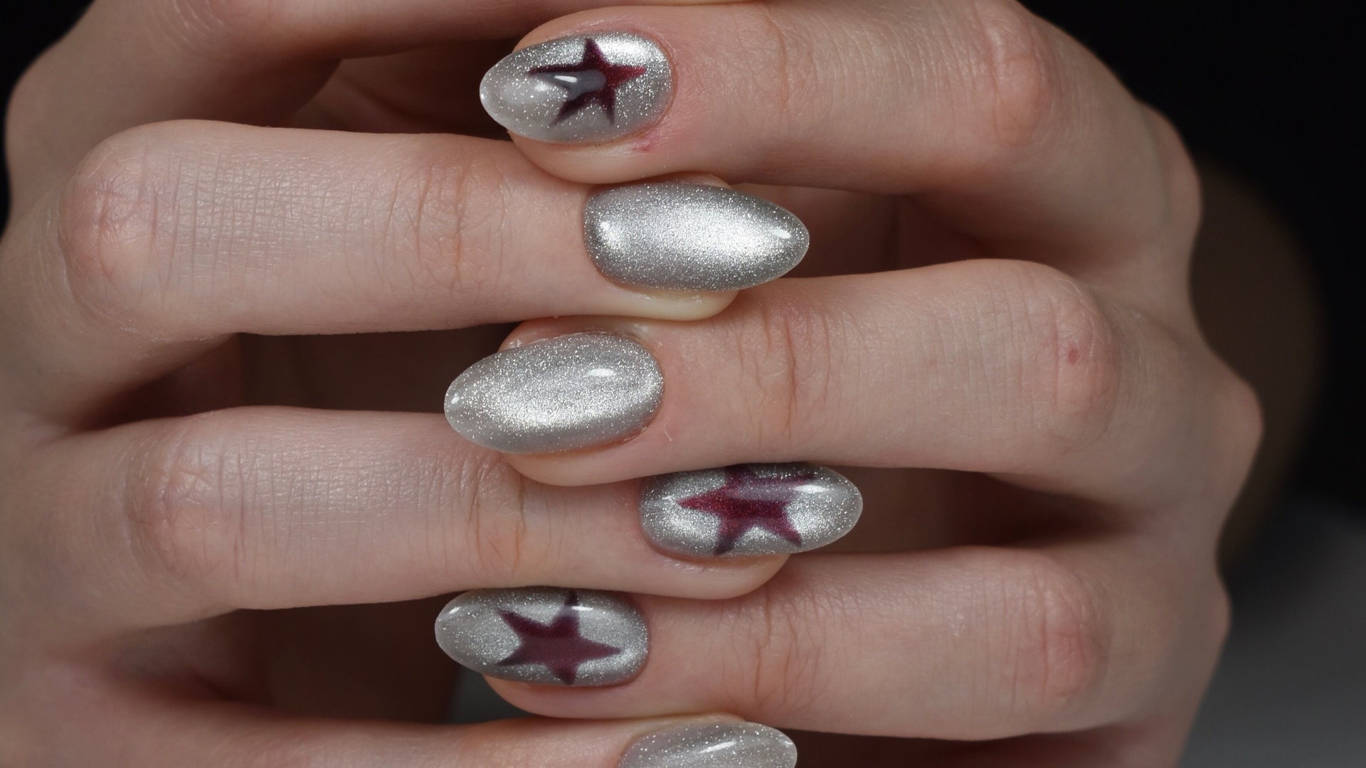 Zilveren chrome nagels met paarse sterren, handen gevouwen voor een donkere achtergrond